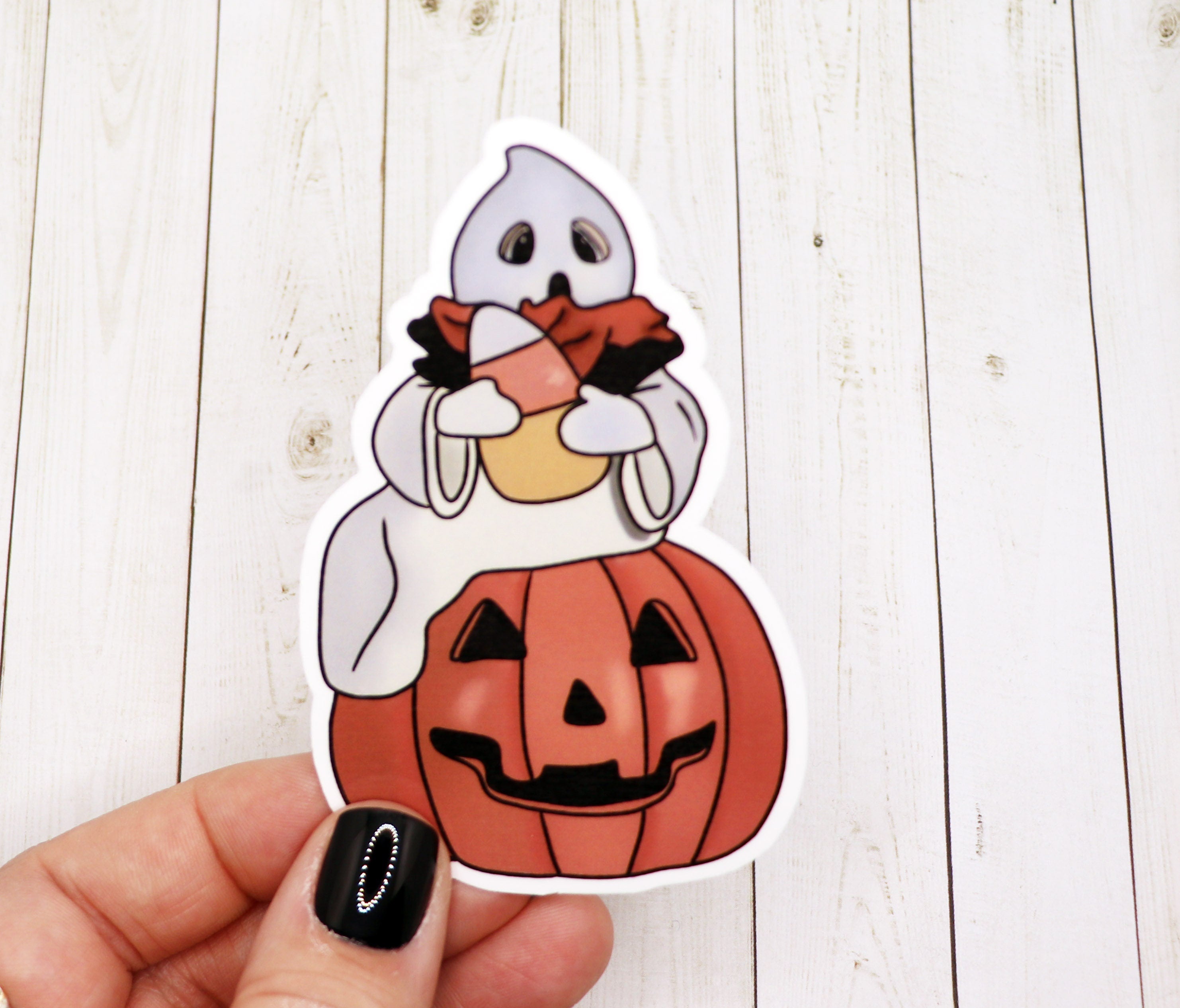 A vibrant pumpkin and ghost sticker on a matte vinyl surface, showcasing Halloween-themed design.