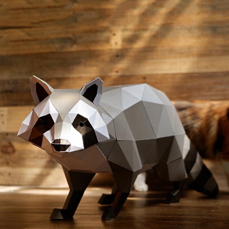 A detailed 3D papercraft raccoon model in grayscale tones, crouched in a sneaky position, showcasing its intricate design and sturdy paper material.