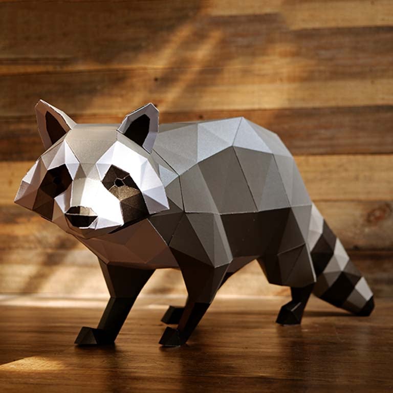 A detailed 3D papercraft raccoon model in grayscale tones, crouched in a sneaky position, showcasing its intricate design and sturdy paper material.