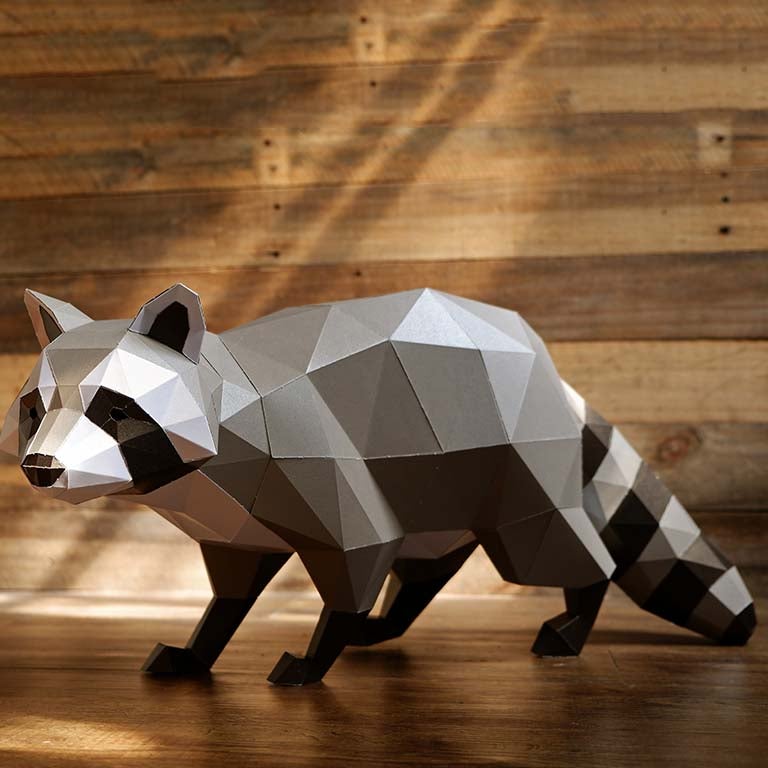 A detailed 3D papercraft raccoon model in grayscale tones, crouched in a sneaky position, showcasing its intricate design and sturdy paper material.