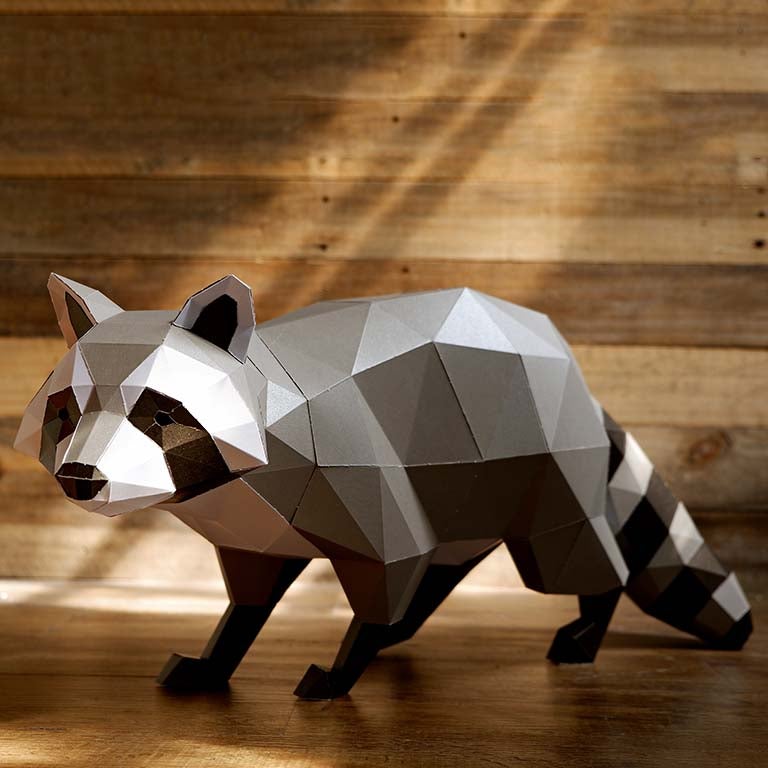 A detailed 3D papercraft raccoon model in grayscale tones, crouched in a sneaky position, showcasing its intricate design and sturdy paper material.