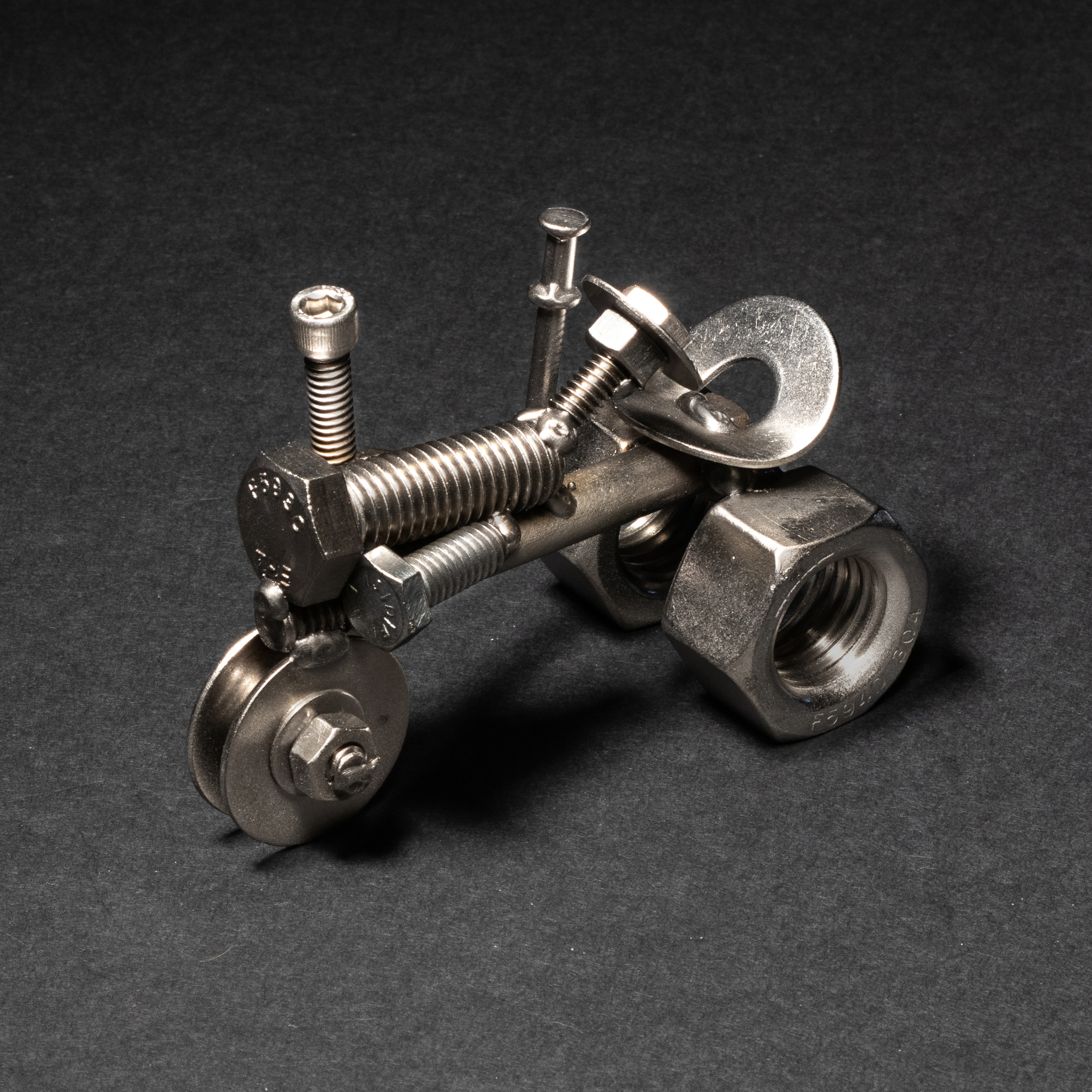 Handmade scrap metal tractor figurine crafted from nuts, bolts, and wire, featuring a rustic design with a protective finish.