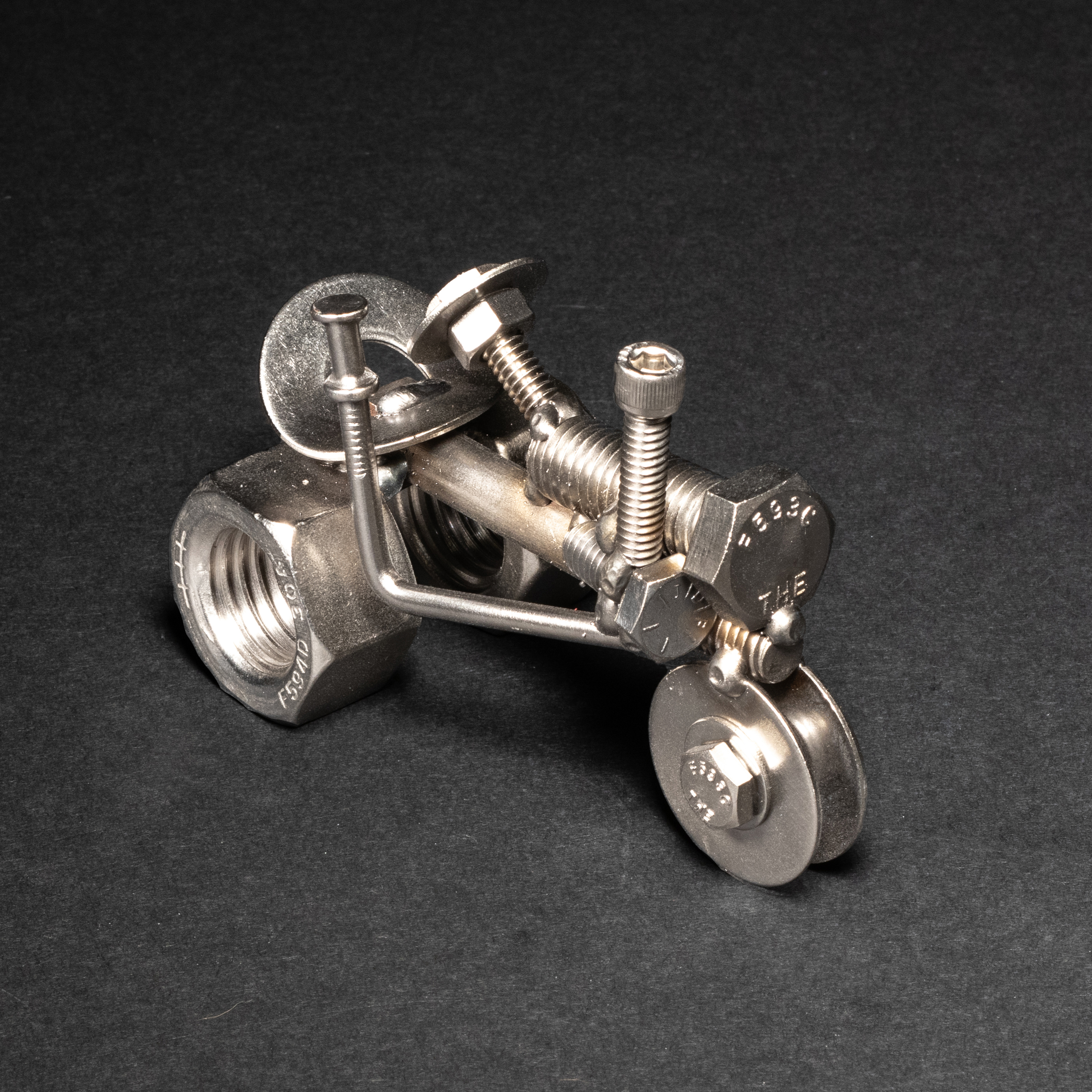 Handmade scrap metal tractor figurine crafted from nuts, bolts, and wire, featuring a rustic design with a protective finish.