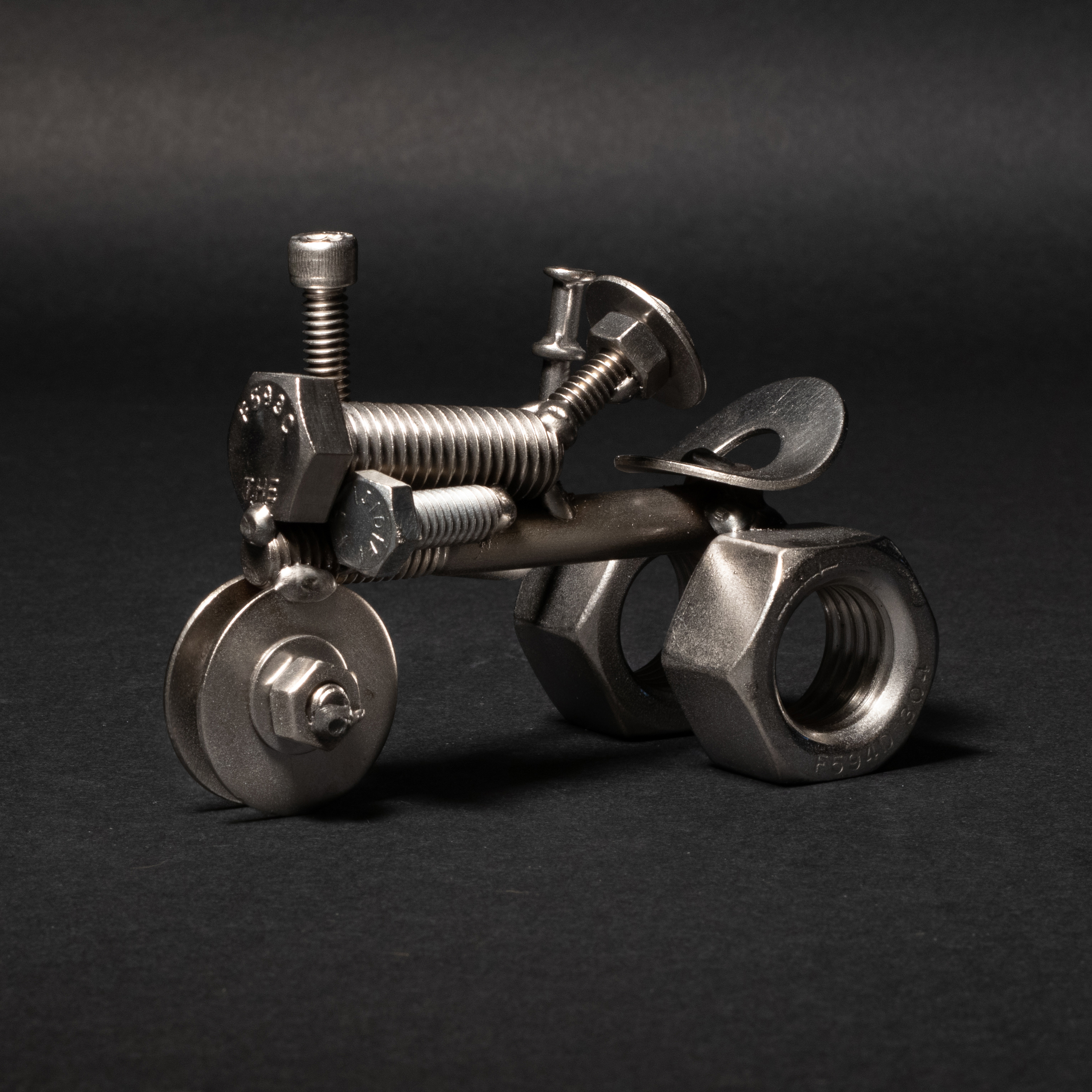 Handmade scrap metal tractor figurine crafted from nuts, bolts, and wire, featuring a rustic design with a protective finish.