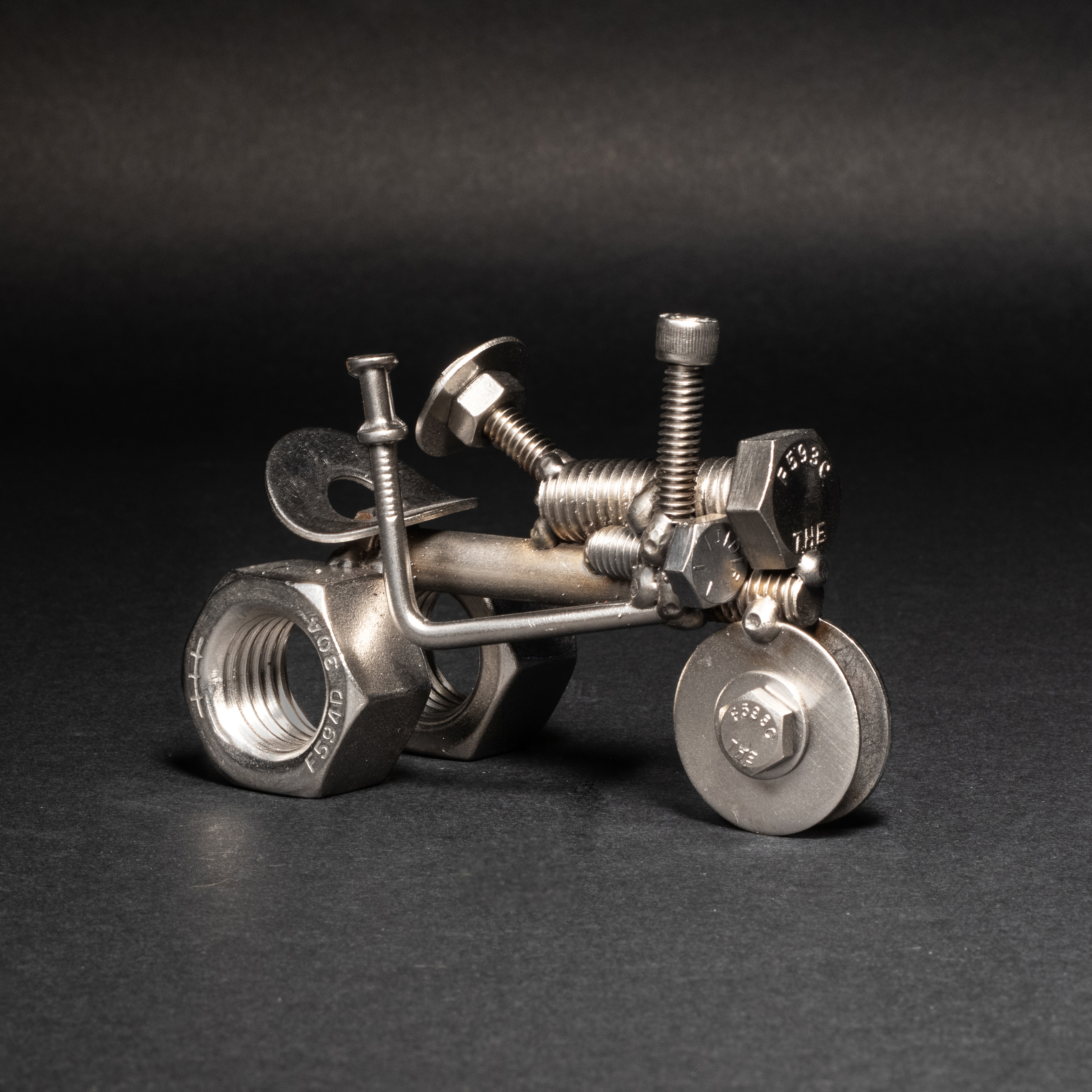 Handmade scrap metal tractor figurine crafted from nuts, bolts, and wire, featuring a rustic design with a protective finish.