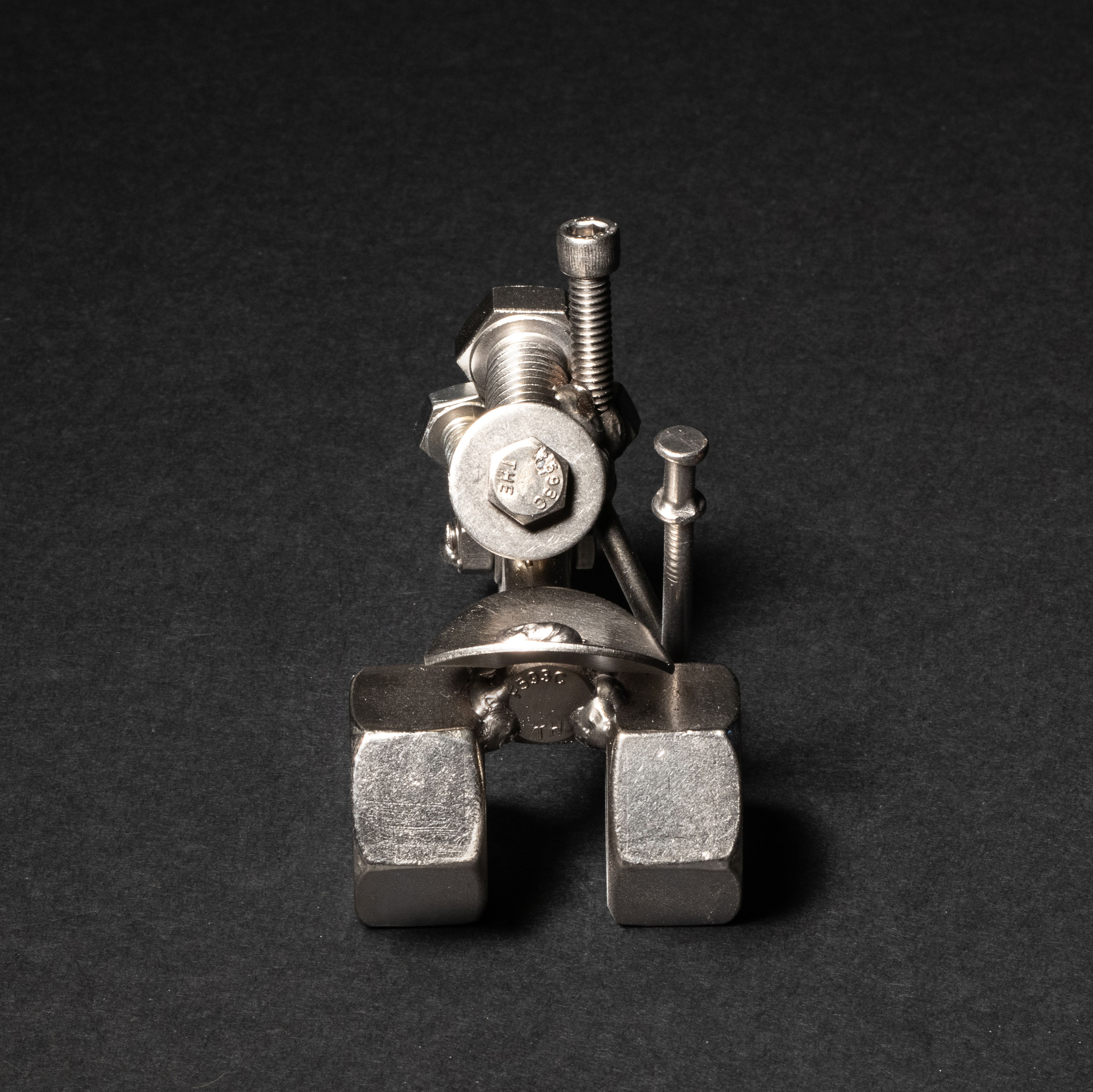 Handmade scrap metal tractor figurine crafted from nuts, bolts, and wire, featuring a rustic design with a protective finish.