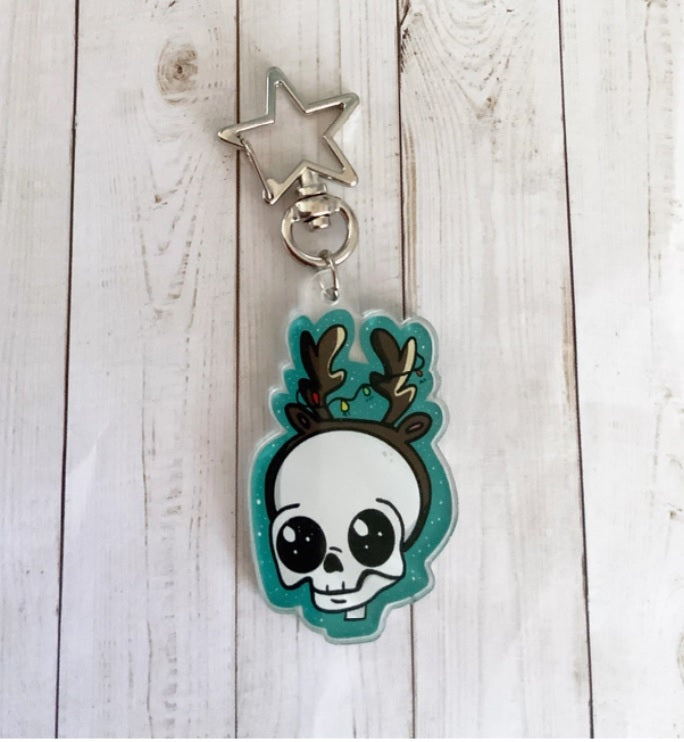 A festive Skull Reindeer Acrylic Keychain featuring a unique illustration, attached to a gold star keyring.