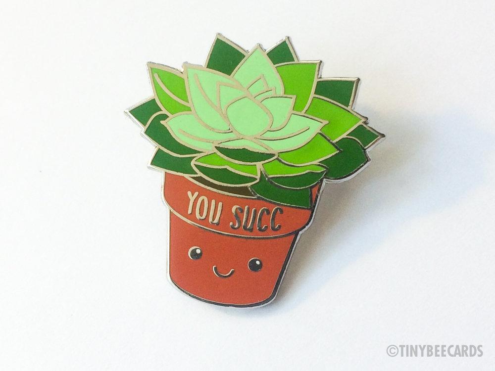 A cute kawaii succulent enamel pin featuring the pun 'You Succ!' with vibrant colors and a silver nickel finish.