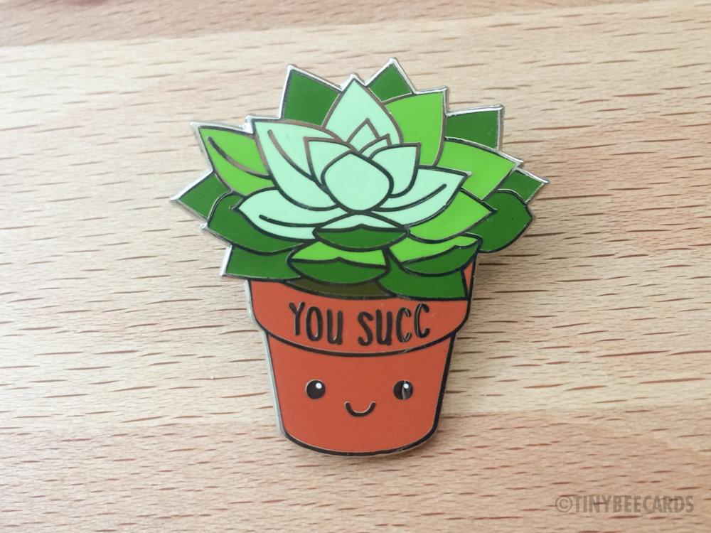 A cute kawaii succulent enamel pin featuring the pun 'You Succ!' with vibrant colors and a silver nickel finish.