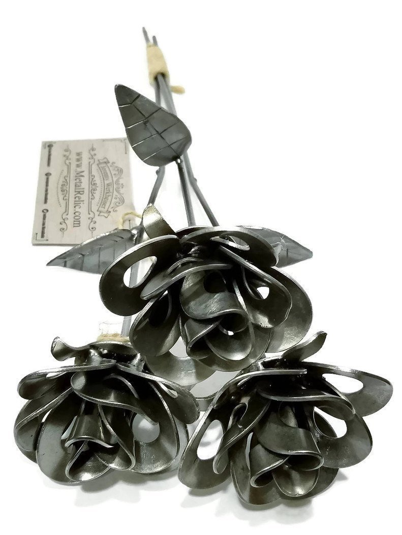 Three handcrafted welded steel roses made from recycled materials, showcasing unique designs and a rustic finish.