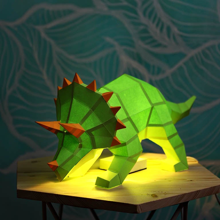 A vibrant green Triceratops 3D paper model lamp with orange horn spikes, showcasing intricate details and a unique design.