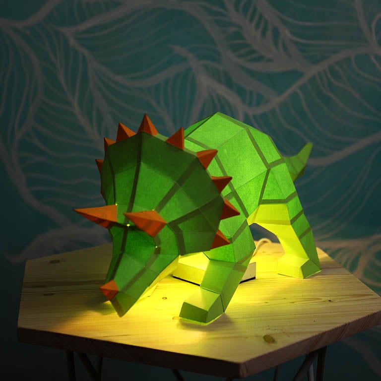 A vibrant green Triceratops 3D paper model lamp with orange horn spikes, showcasing intricate details and a unique design.