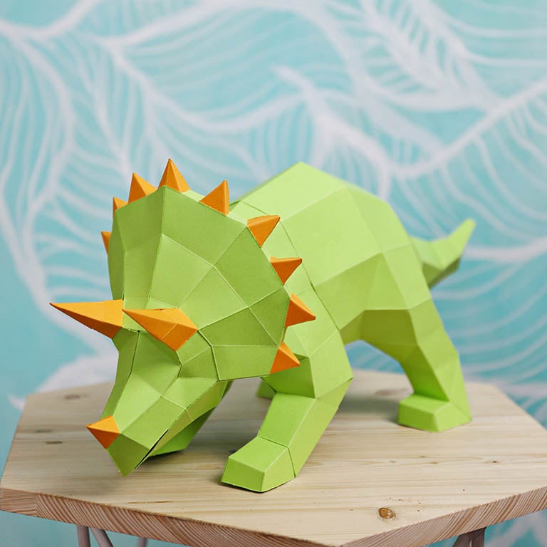 A vibrant green Triceratops 3D paper model lamp with orange horn spikes, showcasing intricate details and a unique design.