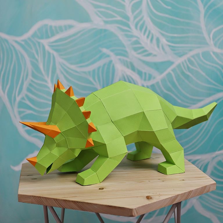 A vibrant green Triceratops 3D paper model lamp with orange horn spikes, showcasing intricate details and a unique design.