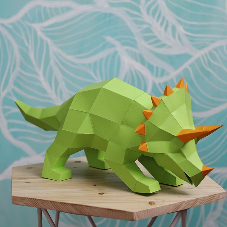 A vibrant green Triceratops 3D paper model lamp with orange horn spikes, showcasing intricate details and a unique design.