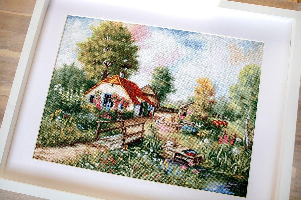 Village landscape counted cross-stitch kit featuring a house, creek, geese, and cows with vibrant colors and detailed design.