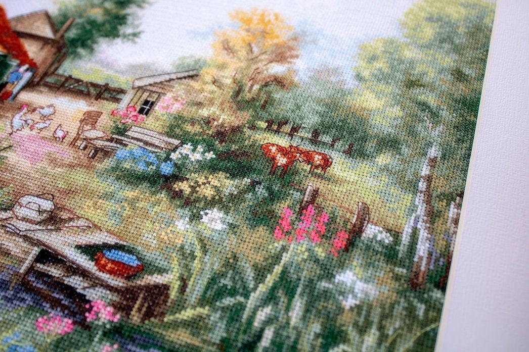 Village landscape counted cross-stitch kit featuring a house, creek, geese, and cows with vibrant colors and detailed design.