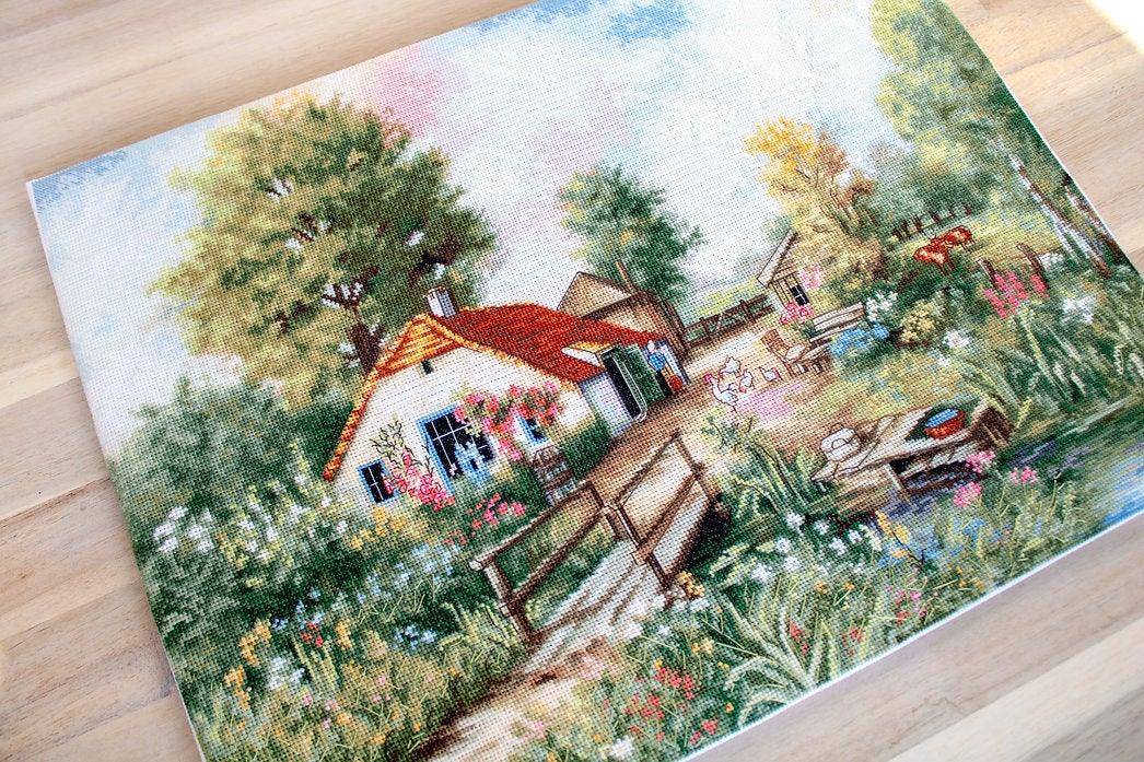 Village landscape counted cross-stitch kit featuring a house, creek, geese, and cows with vibrant colors and detailed design.