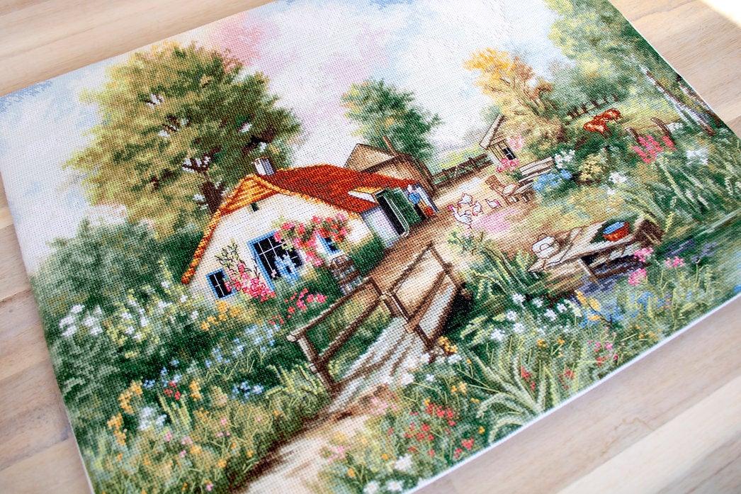 Village landscape counted cross-stitch kit featuring a house, creek, geese, and cows with vibrant colors and detailed design.