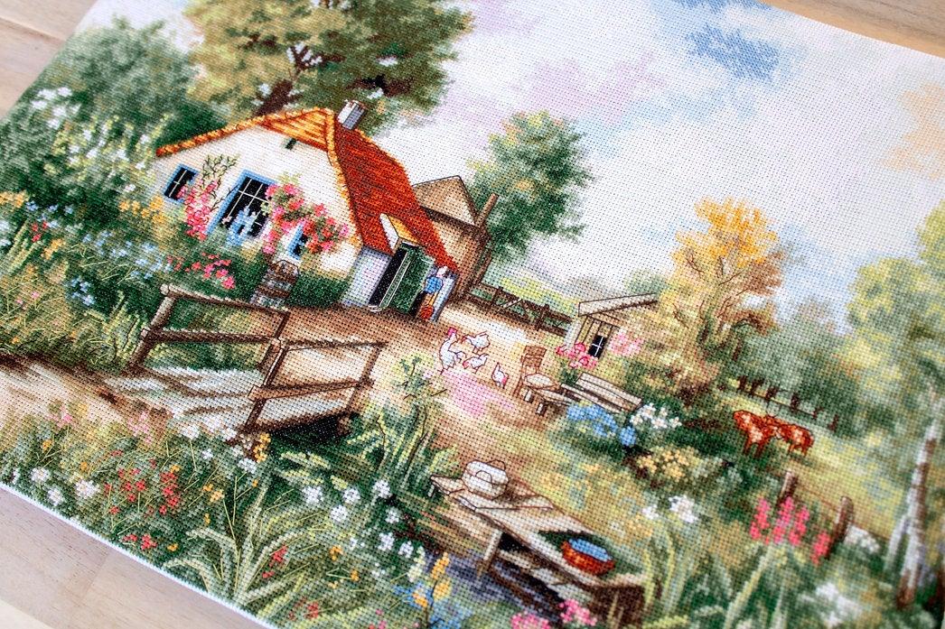 Village landscape counted cross-stitch kit featuring a house, creek, geese, and cows with vibrant colors and detailed design.