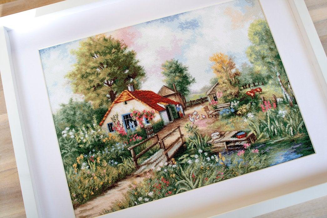 Village landscape counted cross-stitch kit featuring a house, creek, geese, and cows with vibrant colors and detailed design.