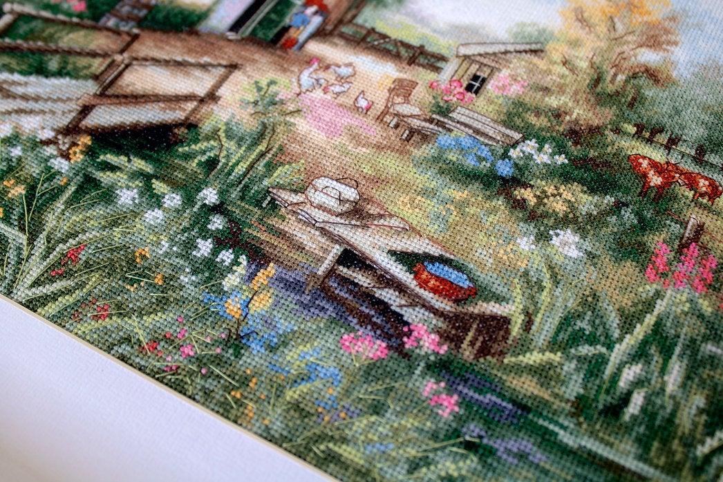 Village landscape counted cross-stitch kit featuring a house, creek, geese, and cows with vibrant colors and detailed design.