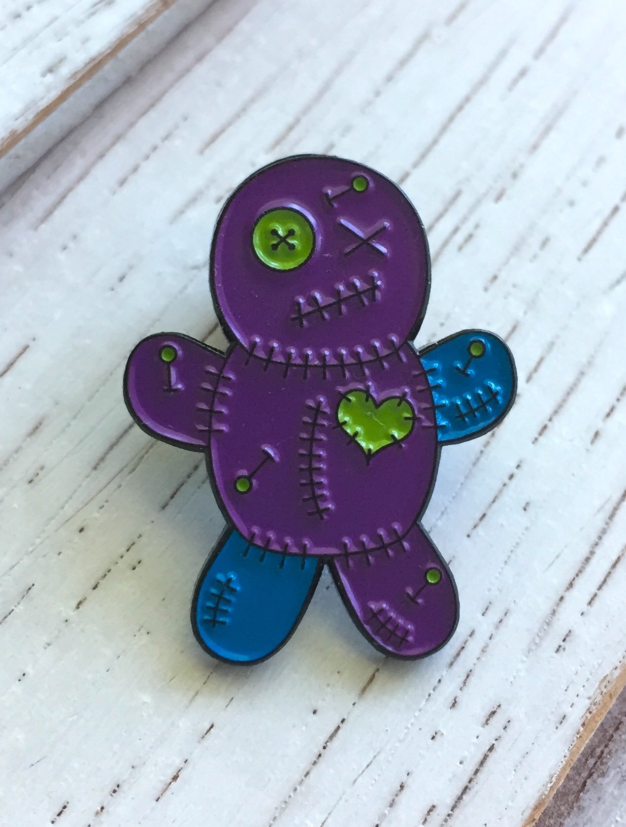 Teal and purple Voodoo Doll soft enamel pin with black metal base, featuring a rubber pin back.