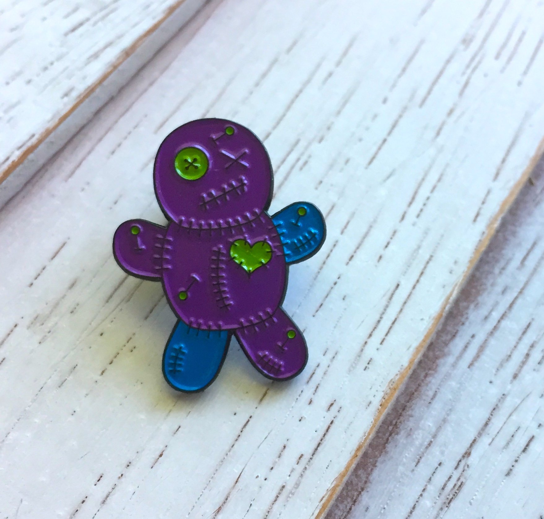 Teal and purple Voodoo Doll soft enamel pin with black metal base, featuring a rubber pin back.