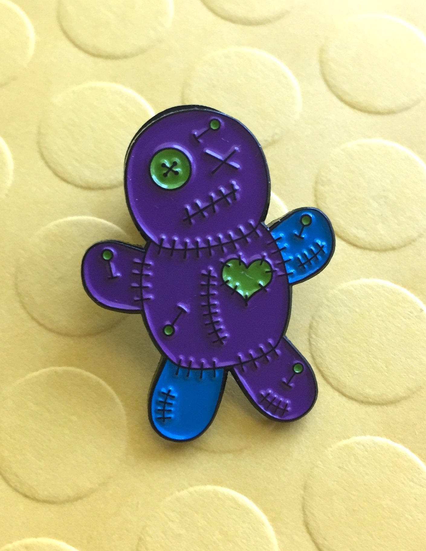 Teal and purple Voodoo Doll soft enamel pin with black metal base, featuring a rubber pin back.