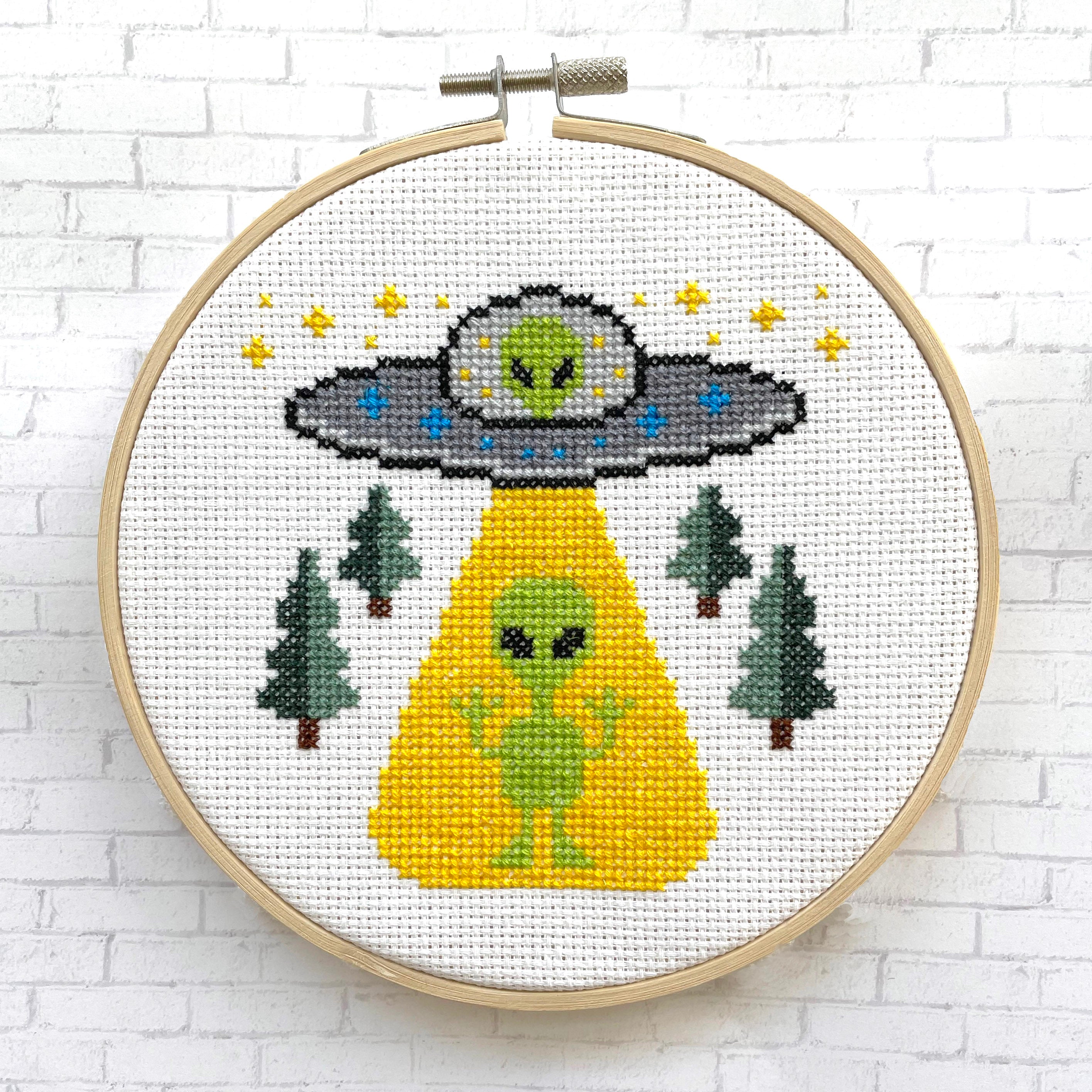 We Are Not Alone Cross Stitch Kit featuring an alien encounter design with included materials like threads and fabric.