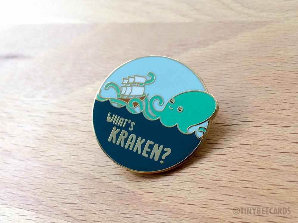 What's Kraken Hard Enamel Pin featuring a cute kraken and ship design on a gold metal background.