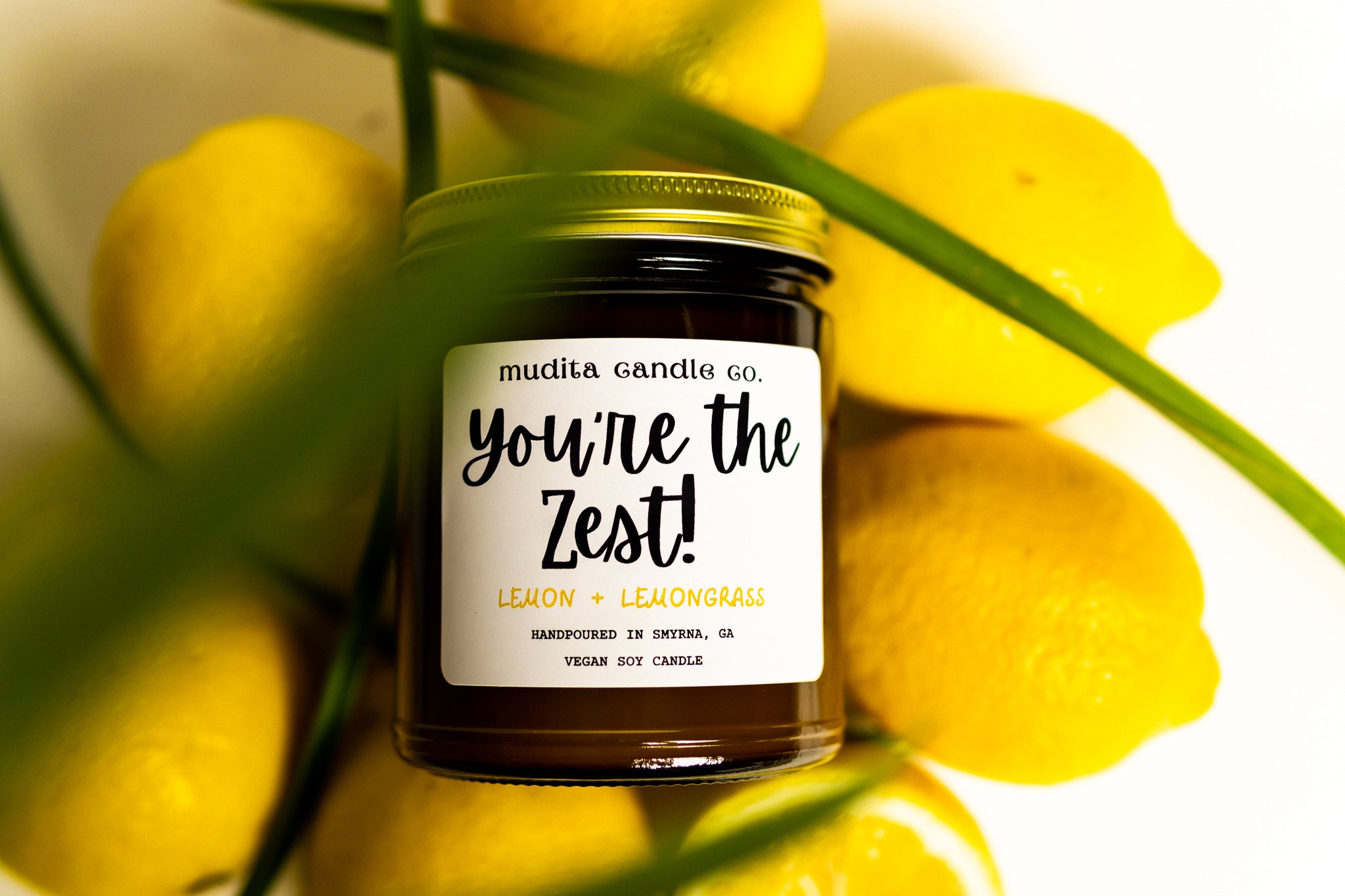 You're the Zest! candle in an amber glass jar with a gold lid, featuring a citrusy lemon and fresh lemongrass scent.