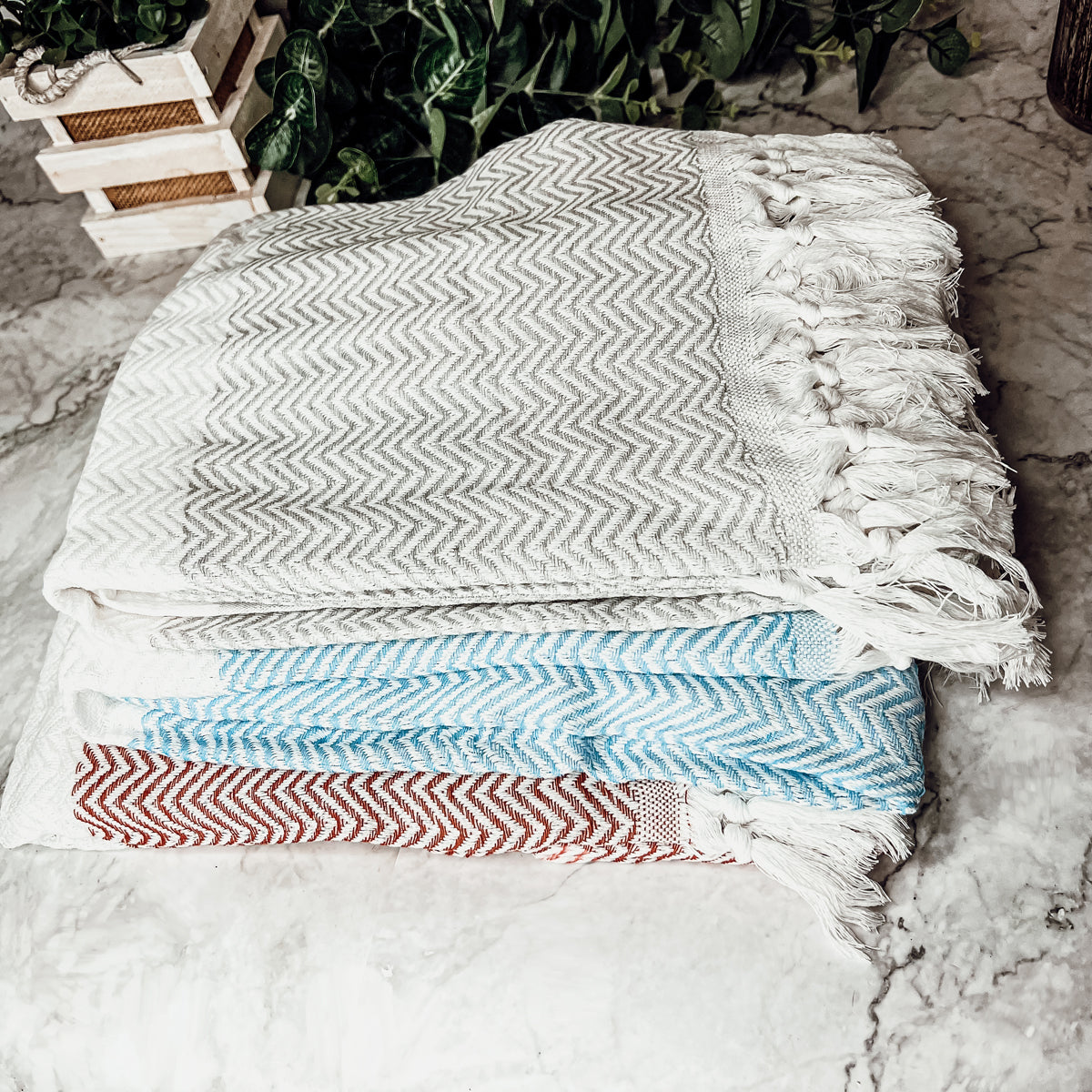 Chevron Towel made from 200 GSM Turkish cotton, featuring decorative tassels and available in blue, gray, and rust colors.