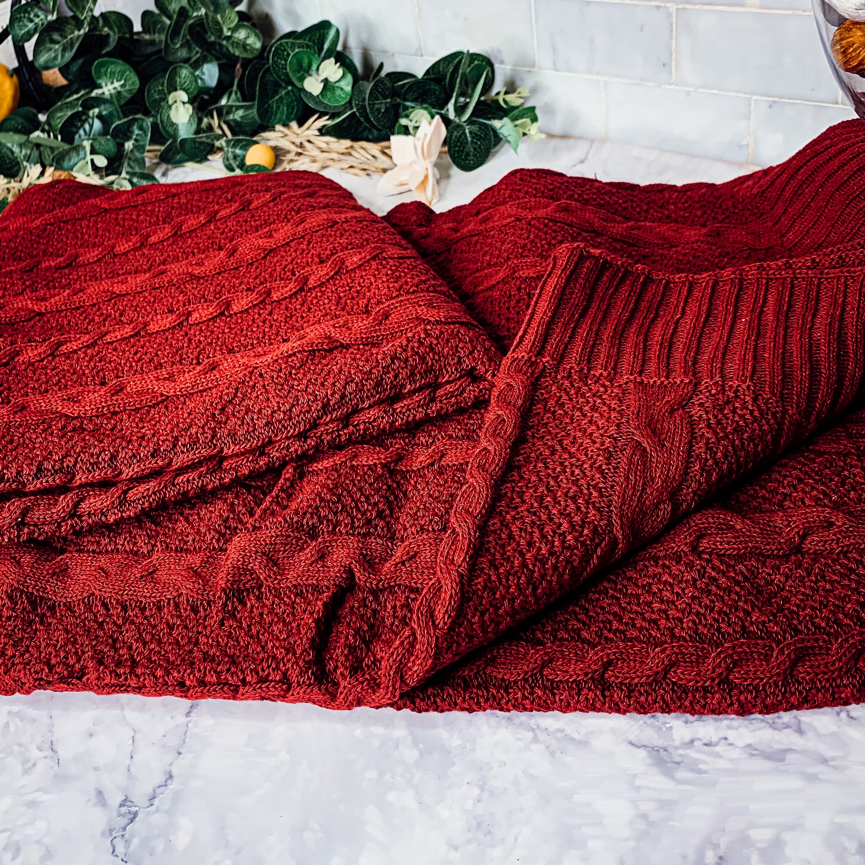 Cozy Claret Knit Sweater Throw blanket draped elegantly on a couch, showcasing its rich color and soft texture.