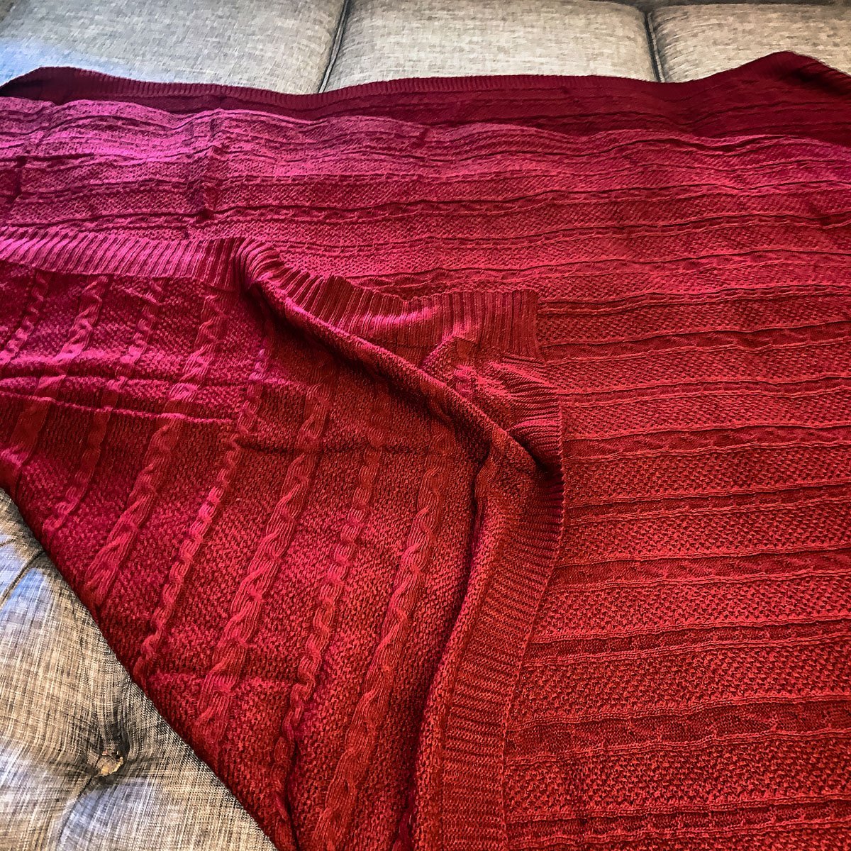 Cozy Claret Knit Sweater Throw blanket draped elegantly on a couch, showcasing its rich color and soft texture.