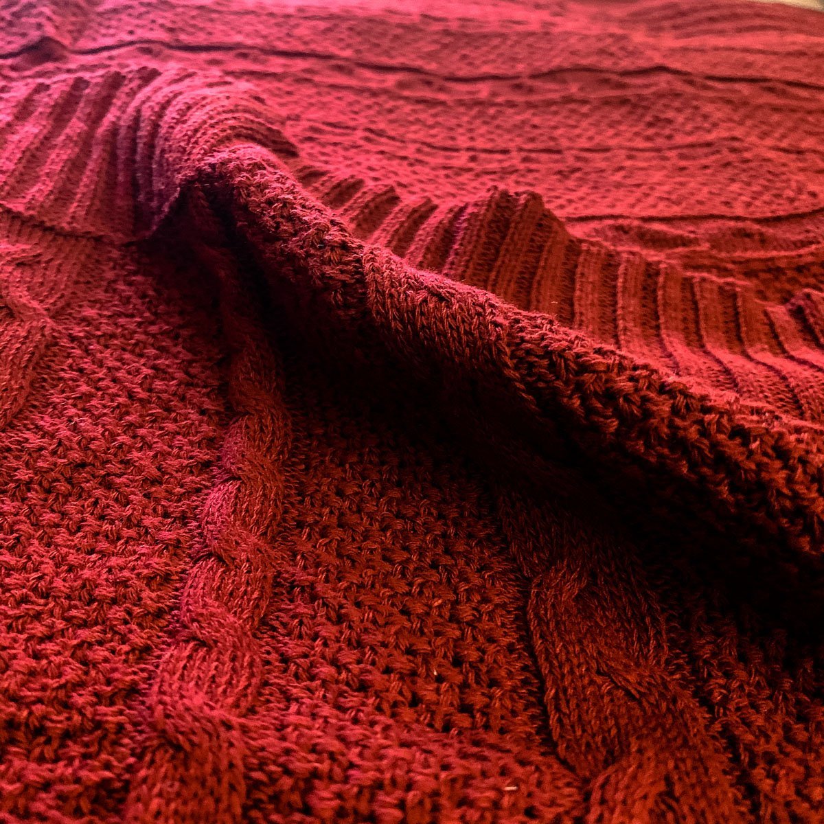 Cozy Claret Knit Sweater Throw blanket draped elegantly on a couch, showcasing its rich color and soft texture.