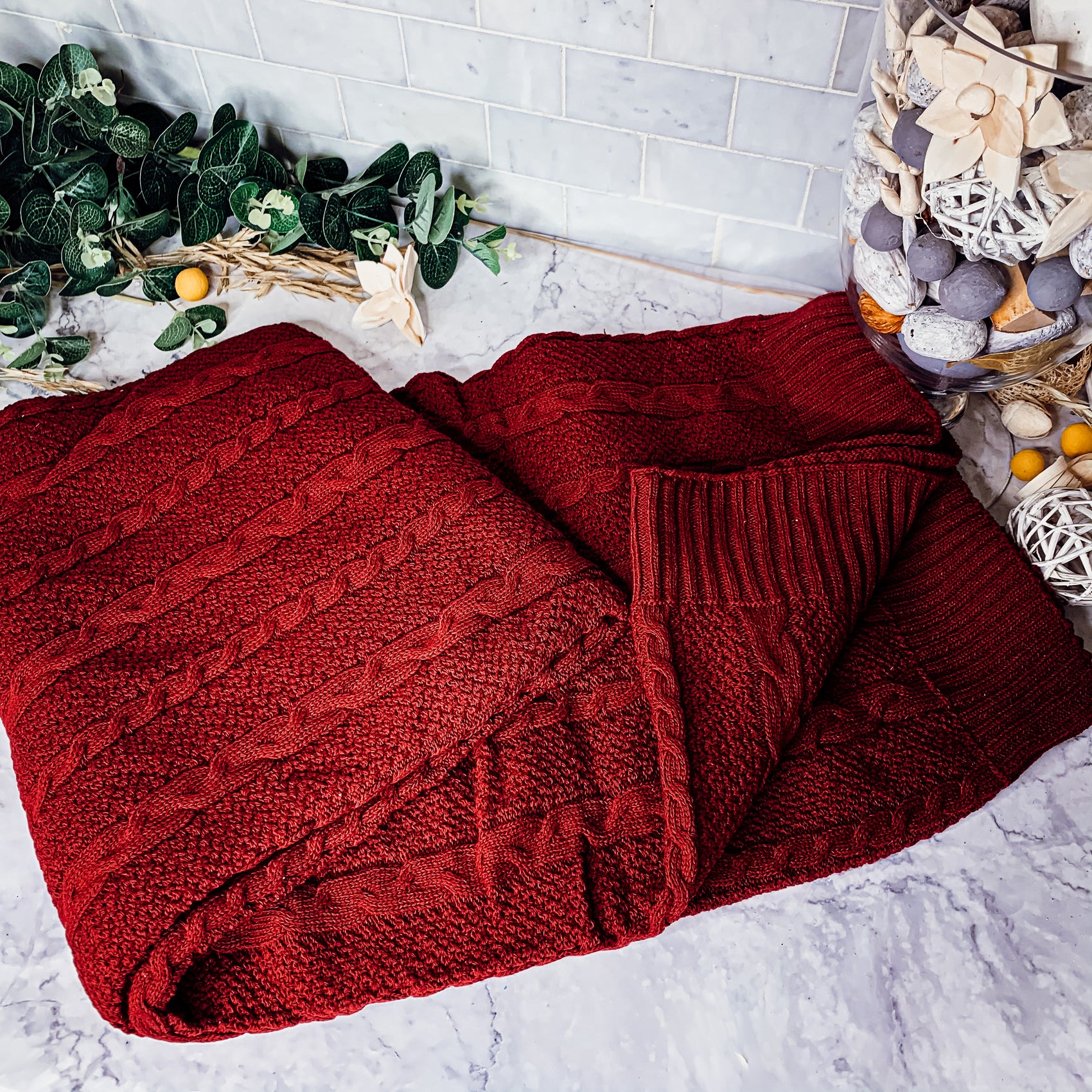 Cozy Claret Knit Sweater Throw blanket draped elegantly on a couch, showcasing its rich color and soft texture.