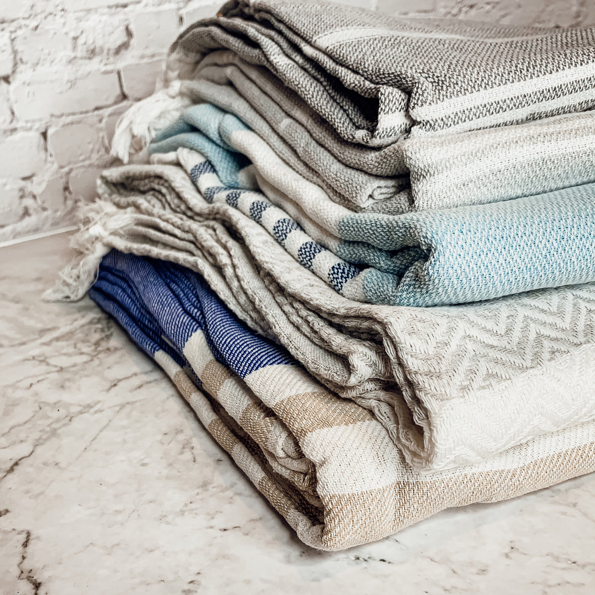 A collection of Mediterranean towels in various colors including light blue, gray, navy, and pink, featuring decorative tassels.