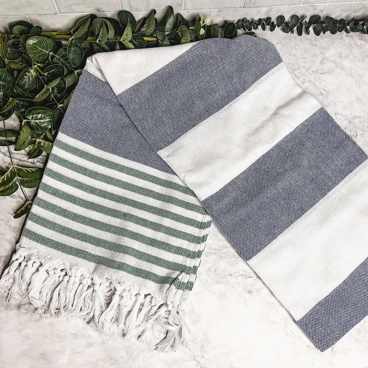 A collection of Mediterranean towels in various colors including light blue, gray, navy, and pink, featuring decorative tassels.