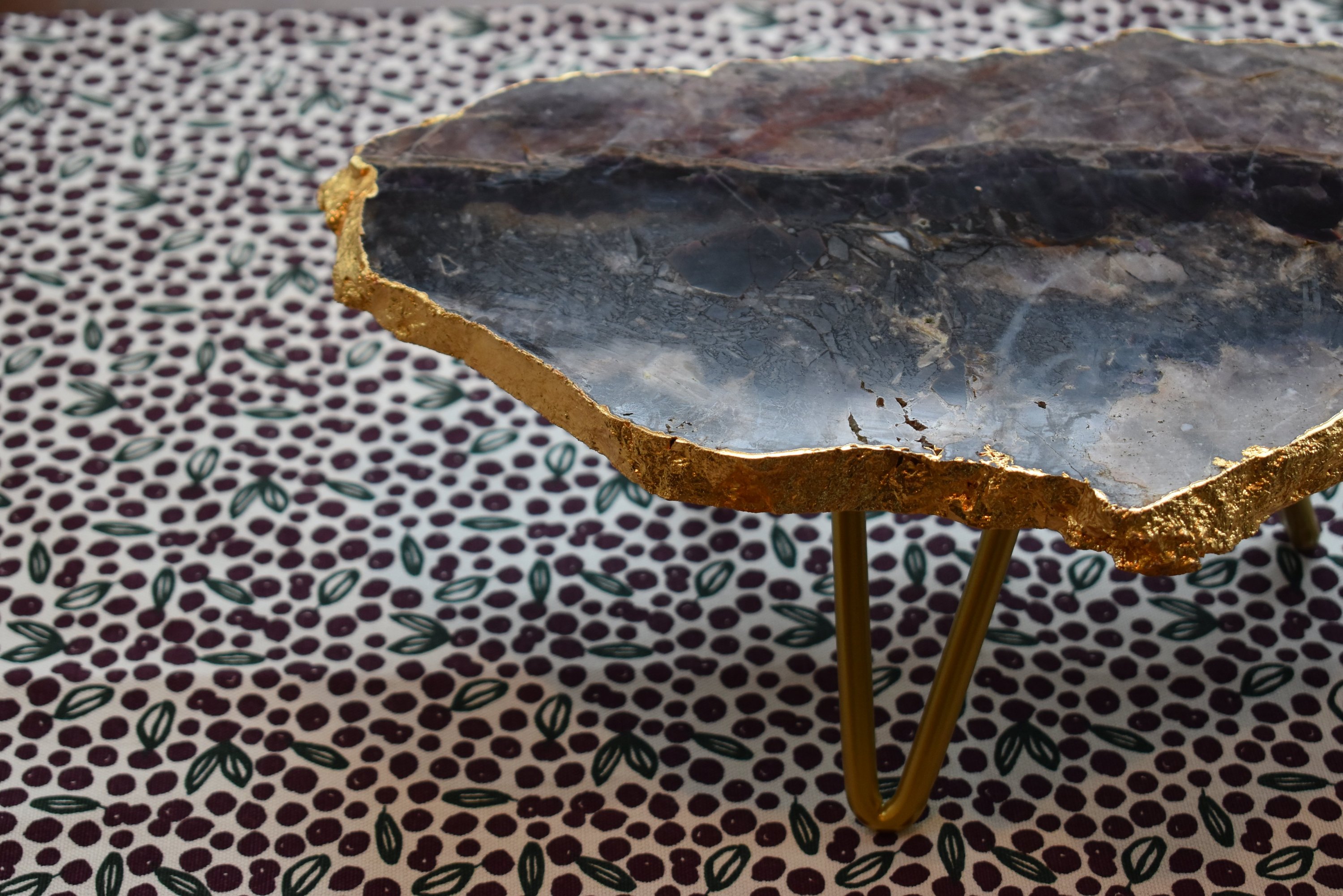 A beautiful 1-layer cake stand featuring unique gemstones like amethyst and rose quartz, accented with elegant gold trim and supported by three golden legs.