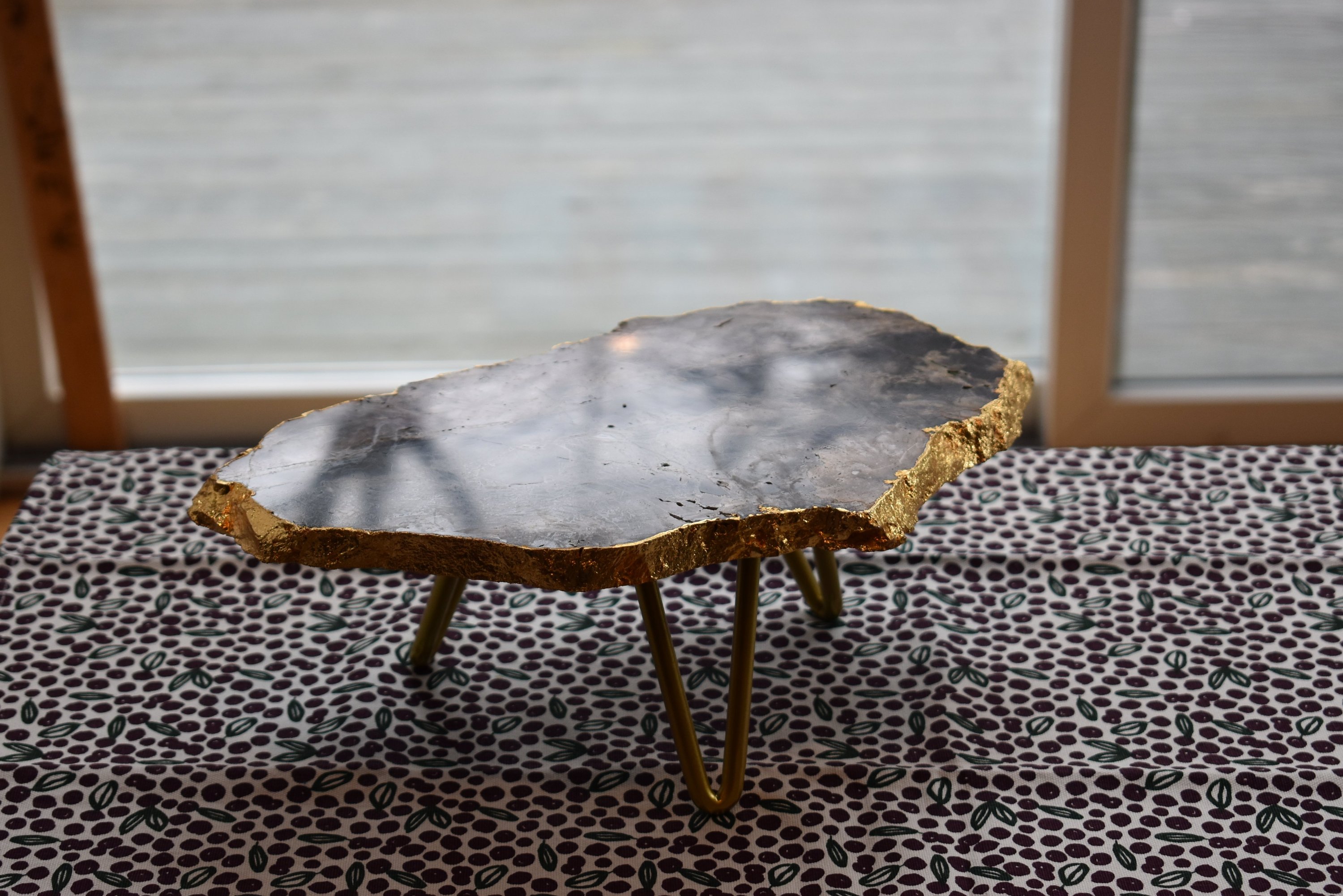 A beautiful 1-layer cake stand featuring unique gemstones like amethyst and rose quartz, accented with elegant gold trim and supported by three golden legs.