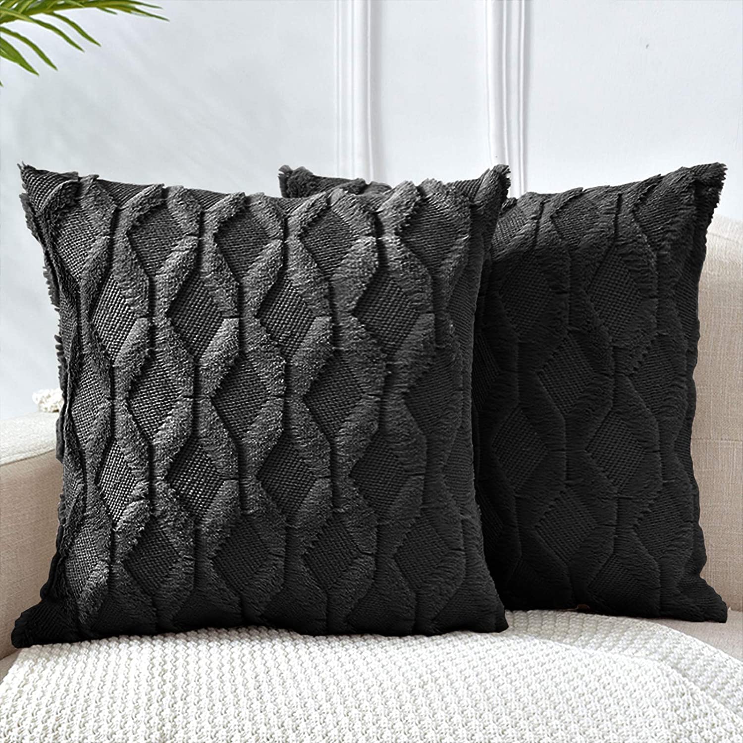 Two black decorative boho throw pillow covers with diamond design, made of soft faux fur and velvet, displayed on a cozy couch.