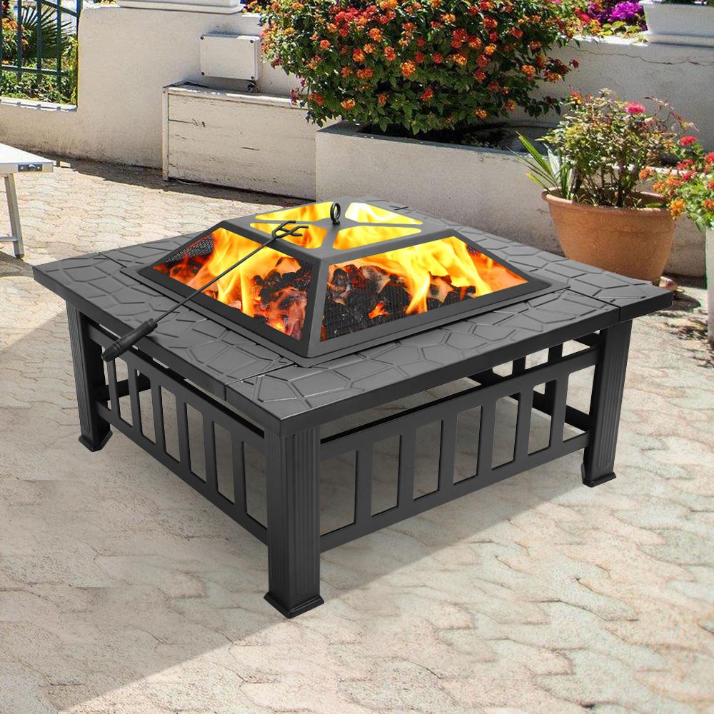 A 32-inch square outdoor garden fire pit BBQ grill with a mesh lid and poker, set on a patio, ideal for warmth and cooking.