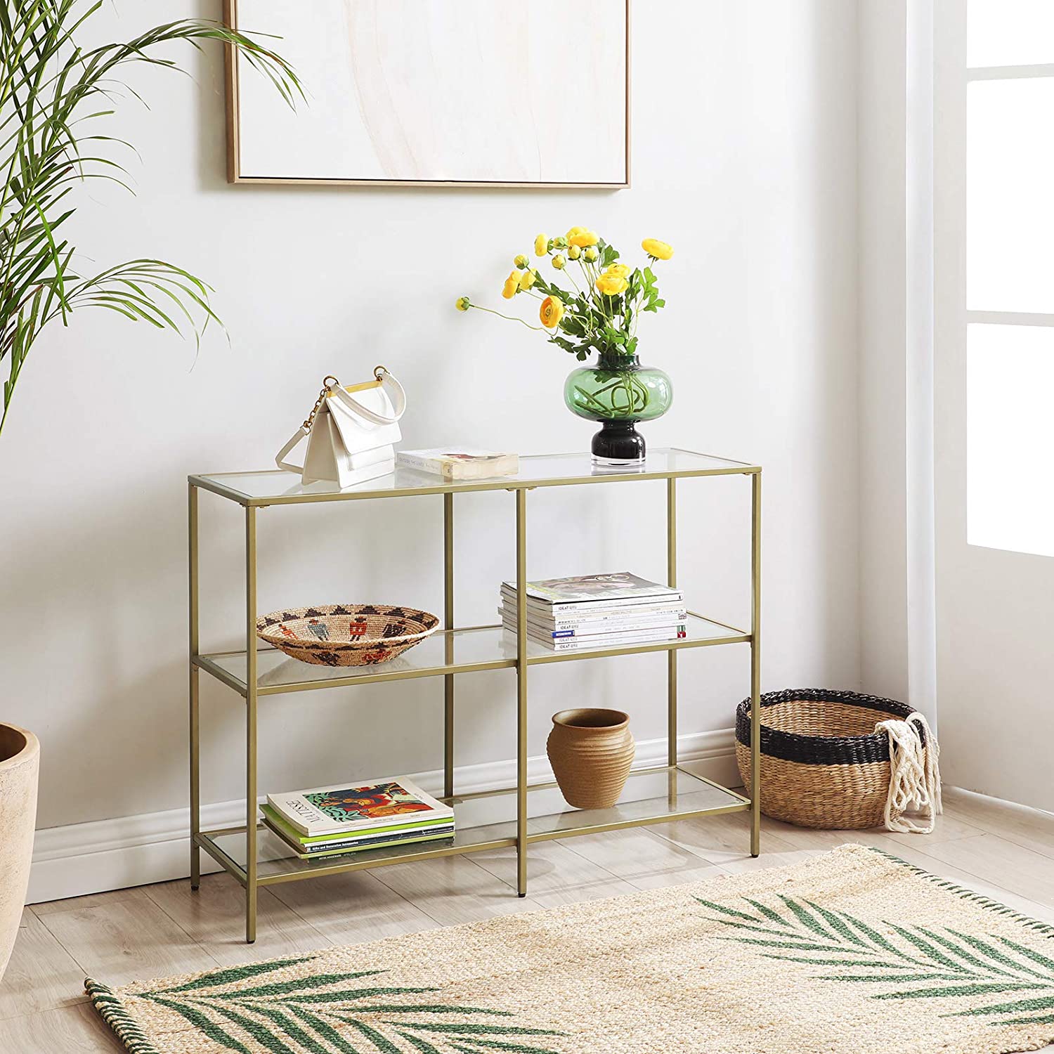 A modern 3-tier tempered glass sofa table with a sleek golden metal frame, showcasing books and decorative plants.