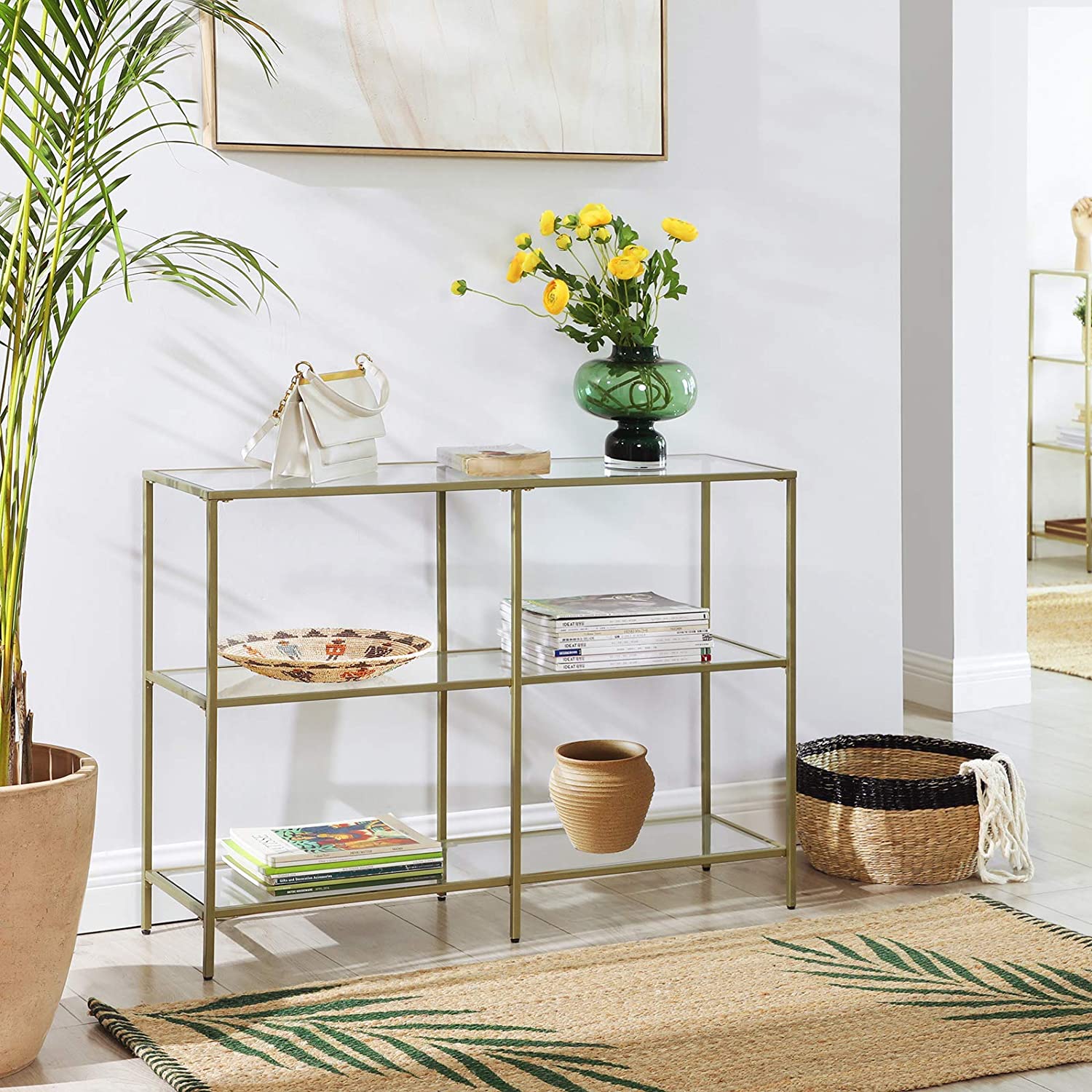 A modern 3-tier tempered glass sofa table with a sleek golden metal frame, showcasing books and decorative plants.