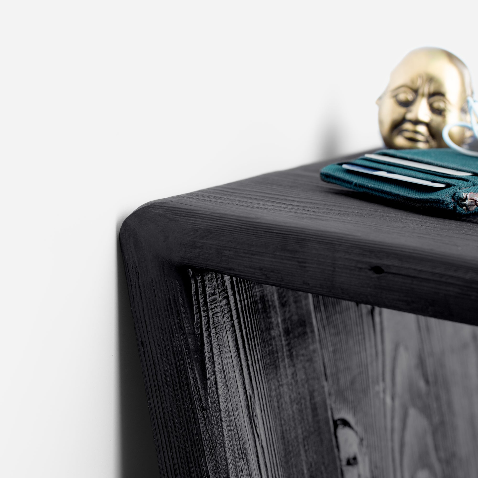 The 7 console table featuring a charred wood finish and brass accent, leaning against a wall, showcasing its unique design.