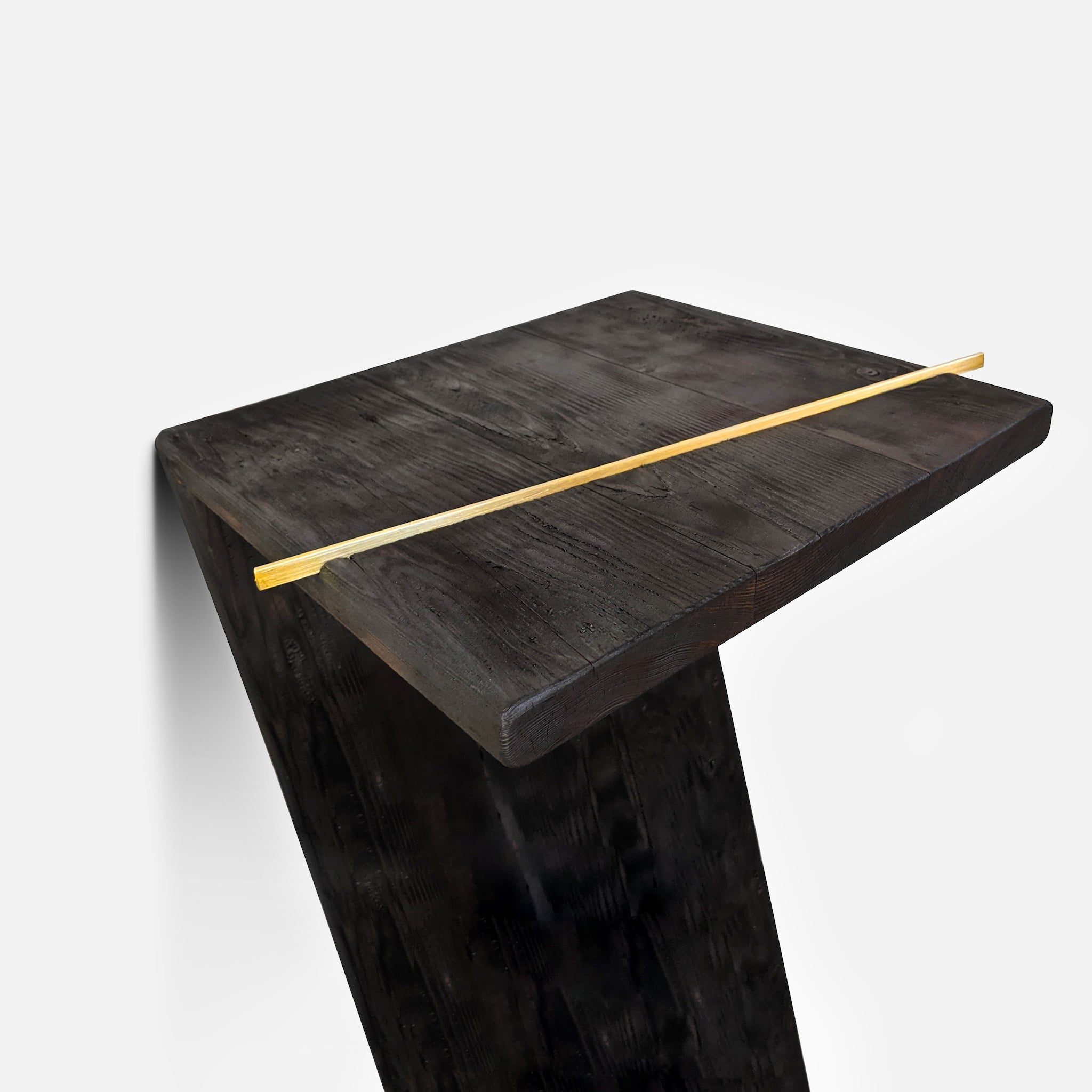 The 7 console table featuring a charred wood finish and brass accent, leaning against a wall, showcasing its unique design.