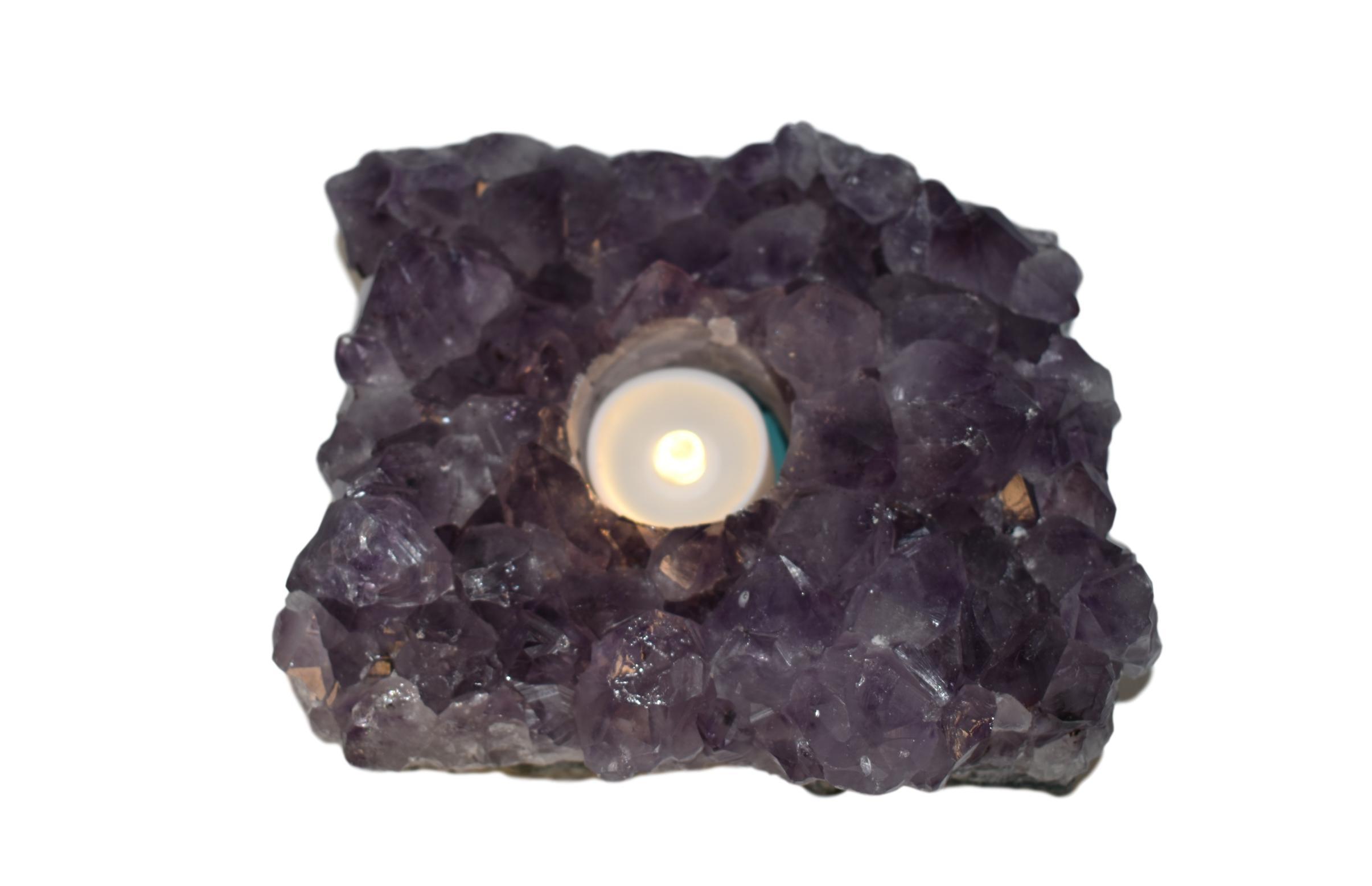 A large natural amethyst votive candle holder with a tea light candle, showcasing its multifaceted surface reflecting soft candlelight.