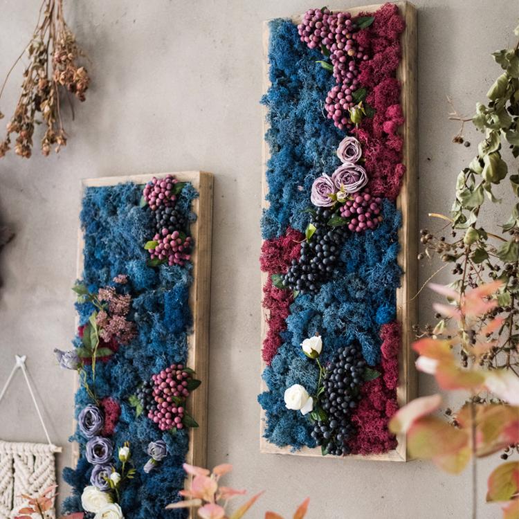 Framed wall art featuring artificial faux silk plants in vibrant blue, purple, pink, and white colors, elegantly arranged in a wooden frame.