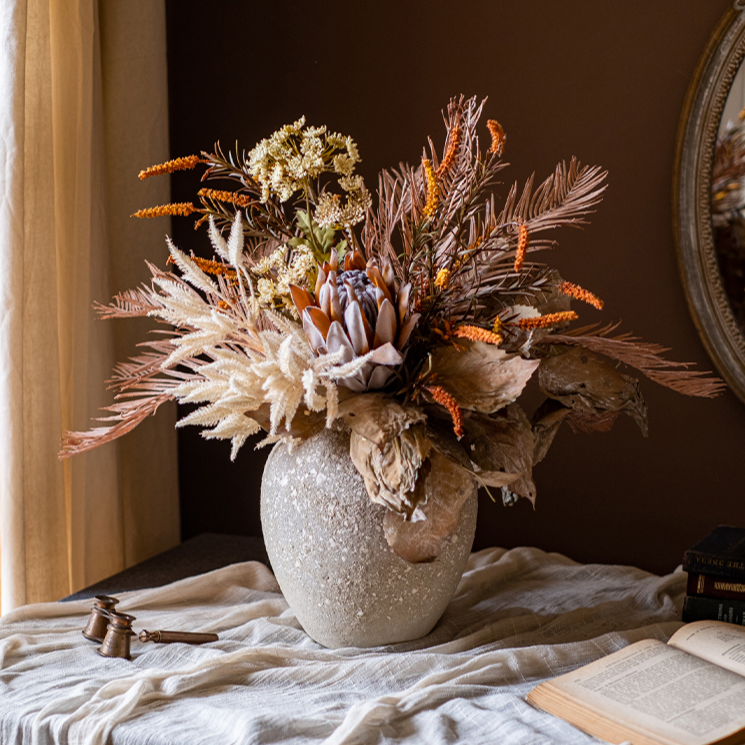 A beautifully arranged Artificial Silk Natural Fall Designer Flower Bouquet featuring protea and fern plants in white, purple, and light brown colors.